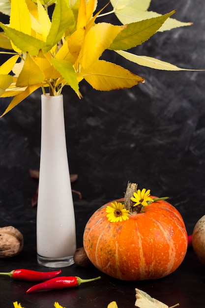 Orange pumpkin on the background of a vase with autumn dry leaves and red peppers garden composition