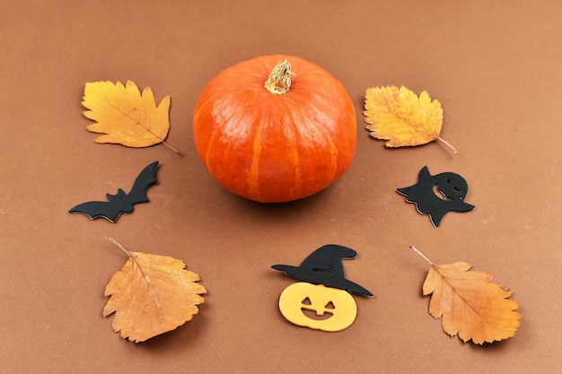 Orange pumpkins lie in a row with autumn leaves on a brown background with Halloween attributes Halloween concept View from above Place for an inscription