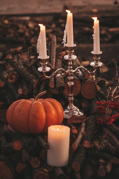 Orange pumpkins with candlestick by three candles among old dry fallen leaves and branches outdoor