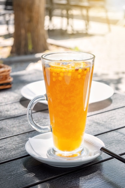 Orange sea buckthorn tea in a glass cup in bright sunlight at a street restaurant. Yellow drink on the table at a park cafe.