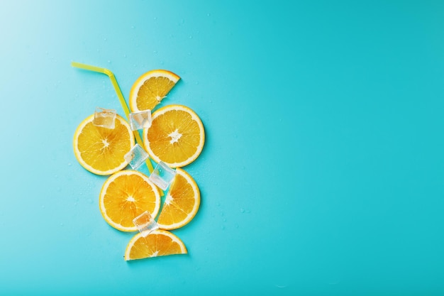 Orange slices and ice cubes with a straw on a blue background in the shape of a cocktail.