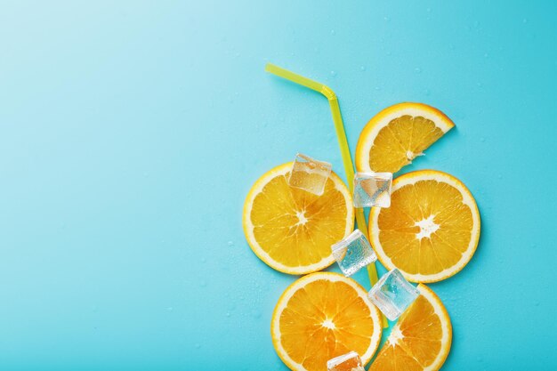 Orange slices and ice cubes with a straw on a blue background in the shape of a cocktail.