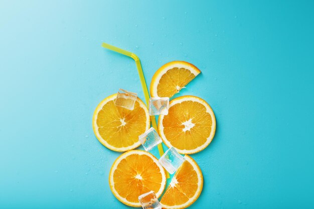 Orange slices and ice cubes with a straw on a blue background in the shape of a cocktail.