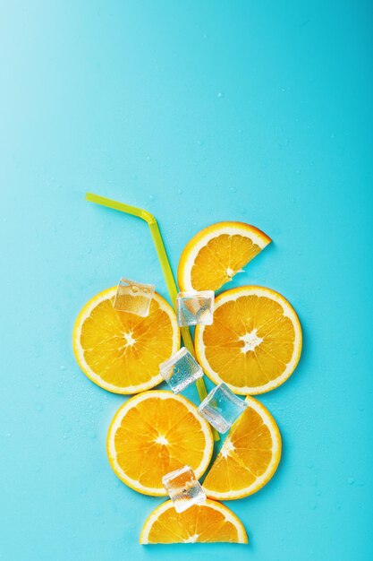 Orange slices and ice cubes with a straw on a blue