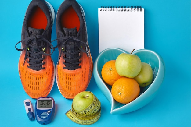 Orange sneakers diary notebook glucometer measuring tape and fruits on a blue background