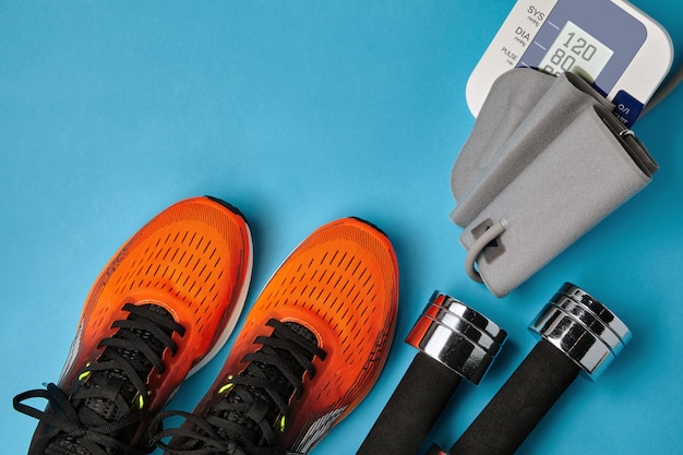 Orange sneakers dumbbells and blood pressure monitor on a blue background