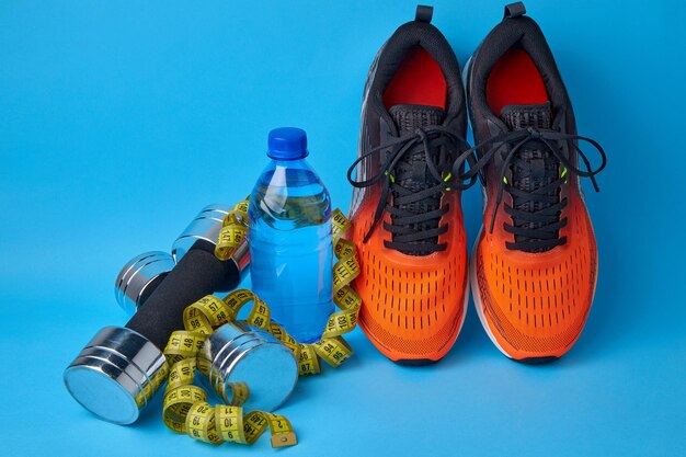 Orange sneakers dumbbells measuring tape and plastic drinking water bottle on a blue background