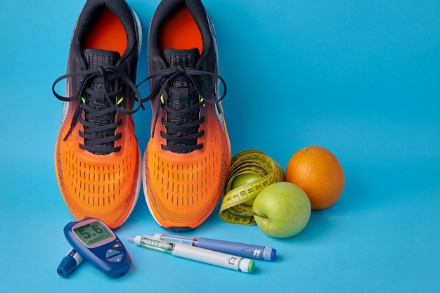 Orange sneakers fruits measuring tape glucometer and insulin syringe pens on a blue background