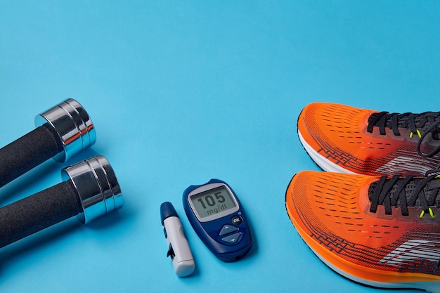 Orange sneakers metal dumbbells and a blood glucose meter on a blue background Exercise to overcome insulin resistance