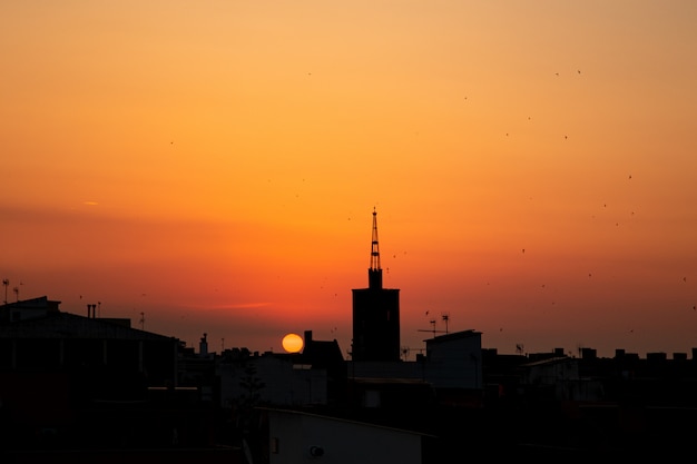 Orange summer sunrise, roof top view of an old church tower above the city.