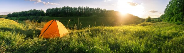 Orange tent in field against background of forest