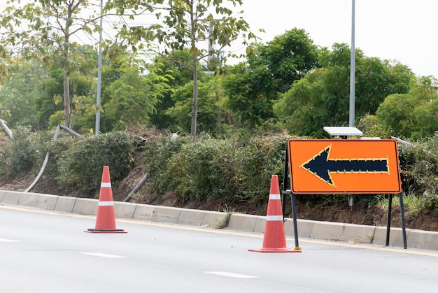 Orange traffic sign with arrow icon and signal cones on highway