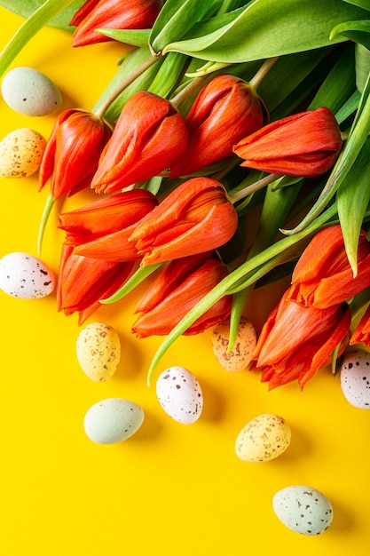 Orange tulips and quail eggs over yellow surface, Easter. Birthday, mother day greeting card concept with copy space. Top view, flat lay