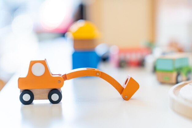 Photo an orange wooden toy excavator is placed on the table in front of other blurry wooden toys