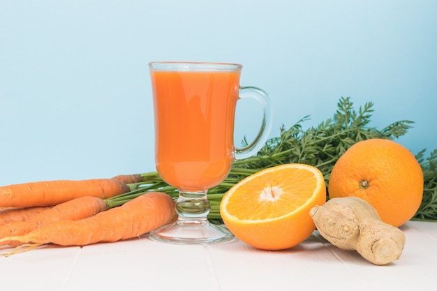 Oranges, ginger, carrots and a glass of smoothies on a wooden table.