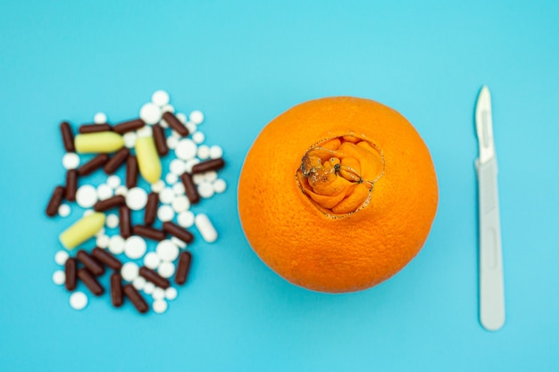 Oranges with a large navel, pills, scalpel on a blue background. concept of medical or surgical treatment of hemorrhoids.