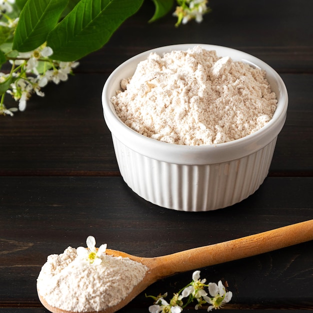 Organic birdcherry flour in a bowl on dark wooden background with a branch of blooming birdcherry