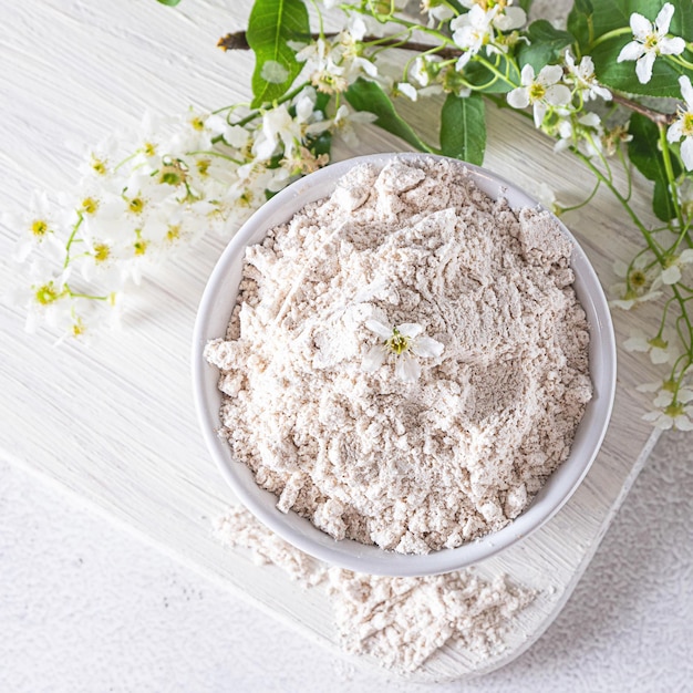 Organic birdcherry flour in a bowl on light grey background with a branch of blooming birdcherry