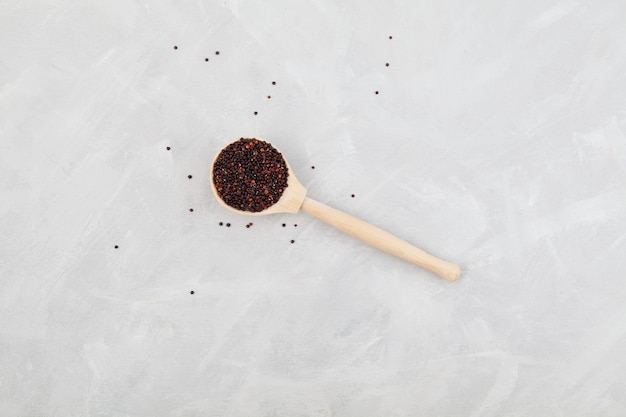 Organic black quinoa in wooden spoon on light grey background. Top view, copy space.