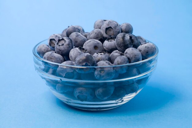 Organic blueberries in glass bowl on blue background front view concept of vegan freshness natural