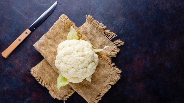 Organic cauliflower on dark background Head of cauliflower on burlap and knife Top view Copy space