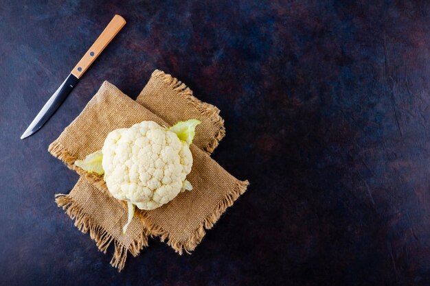 Organic cauliflower on dark background Head of cauliflower on burlap and knife Top view Copy space