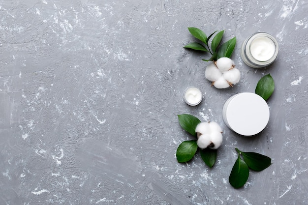 Organic cosmetic products with cotton flower and green leaves on cement background Copy space flat lay