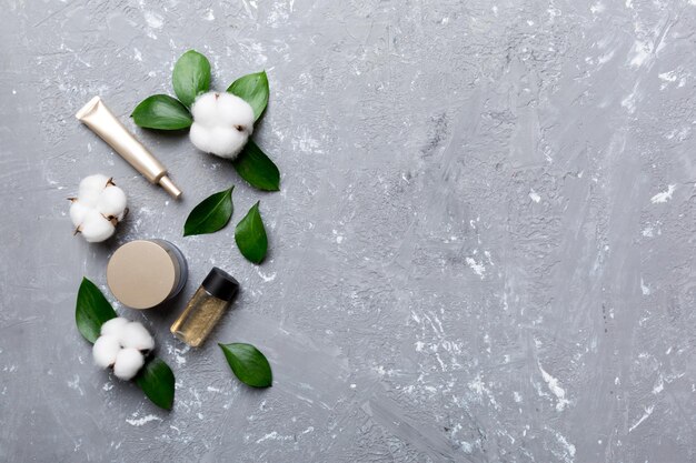 Organic cosmetic products with cotton flower and green leaves on cement background Copy space flat lay