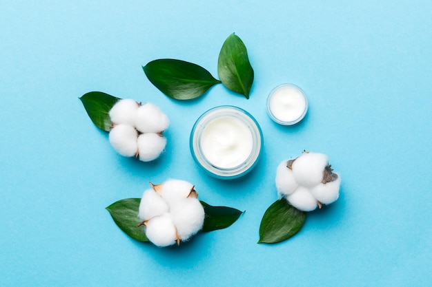 Organic cosmetic products with cotton flower and green leaves on color background Flat lay