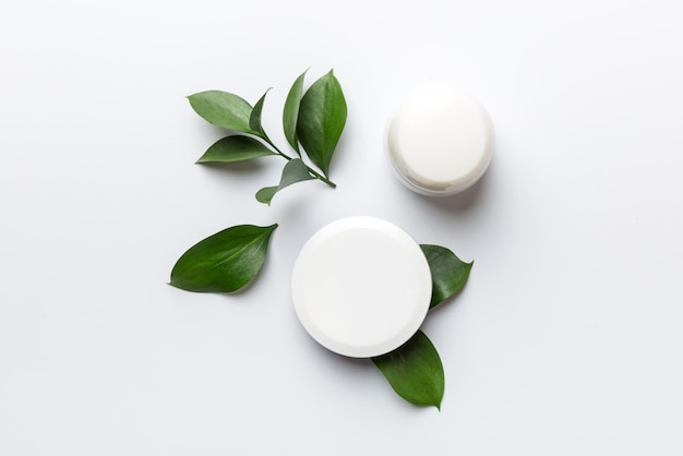 Organic cosmetic products with green leaves on white background Flat lay