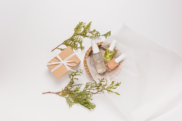 Organic cosmetics with plant and gifts for the holiday. Flat lay, top view clear glass pump bottle, brush jar, moisturizing serum jar in a paper basket on a white background. Natural cosmetics SPA