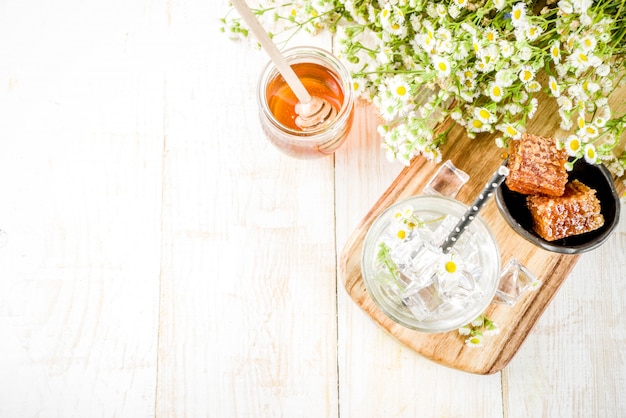 Organic diet detox summer beverage, infused water drink with camomile and honey, on white wooden table, with chamomile flowers and honey in a jar. Copy space