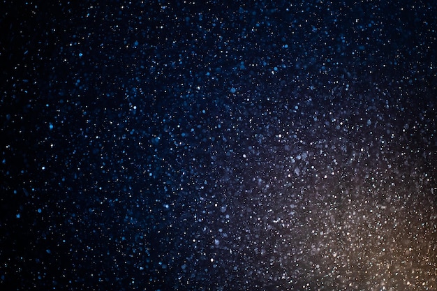 Organic dust particles floating on a colorful light beam on black background. Glowing futuristic.