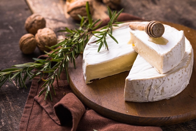 Organic farm camembert or brie cheese on a wooden board with rosemary and nuts, honey.