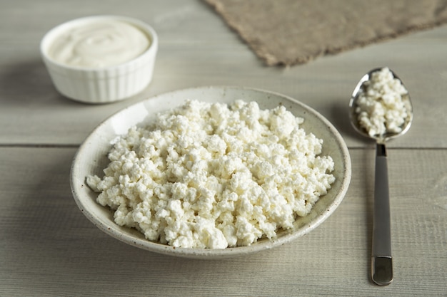 Organic food dairy products sour cream cottage cheese in white utensils on wooden background close up