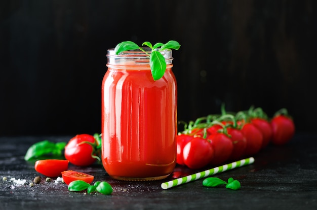 Organic fresh tomato juice in a glass jar, basil, cherry, salt, pepper and straw on dark black. Clean eating and diet concept.