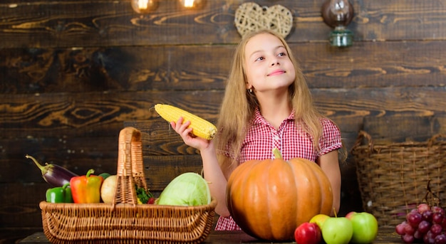 Organic gardening Kid farmer with harvest wooden background Harvest festival concept Girl kid at farm market with organic vegetables Child little girl enjoy farm life Grow your own organic food