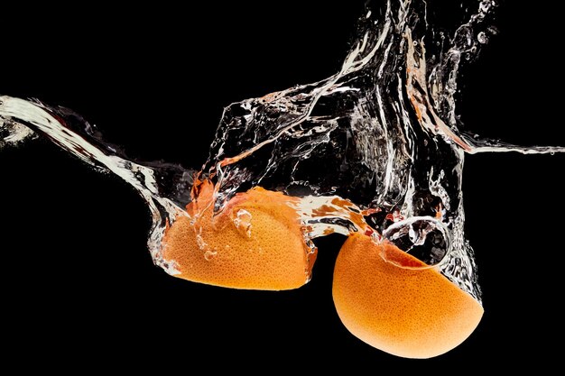 Organic grapefruit halves falling in water with splash isolated on black