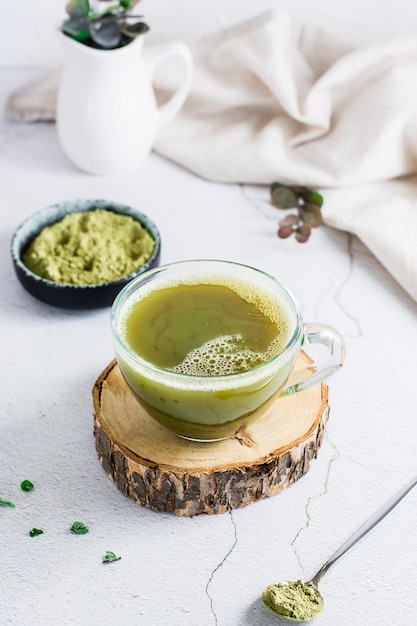 Organic green matcha tea in a cup on a tree trunk on the table Source of vitamins and antioxidants Vertical view Closeup