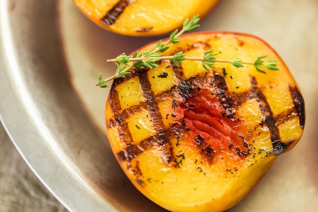 Organic grilled peaches with fresh thyme on a metal plate.