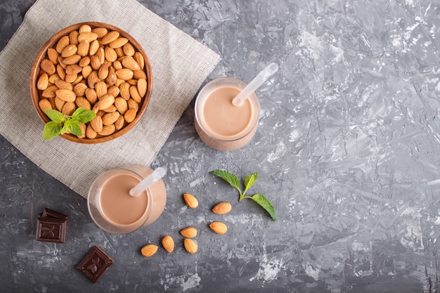 Organic non dairy almond chocolate milk in glass and wooden plate with almond nuts on a black concrete. 