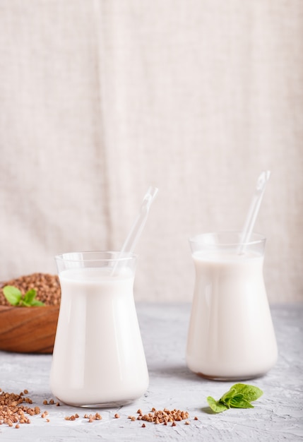 Organic non dairy buckwheat milk in glass and wooden plate on a gray concrete. 