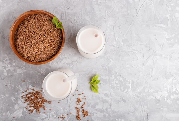 Organic non dairy buckwheat milk in glass and wooden plate with buckwheat seeds on a gray concrete. 