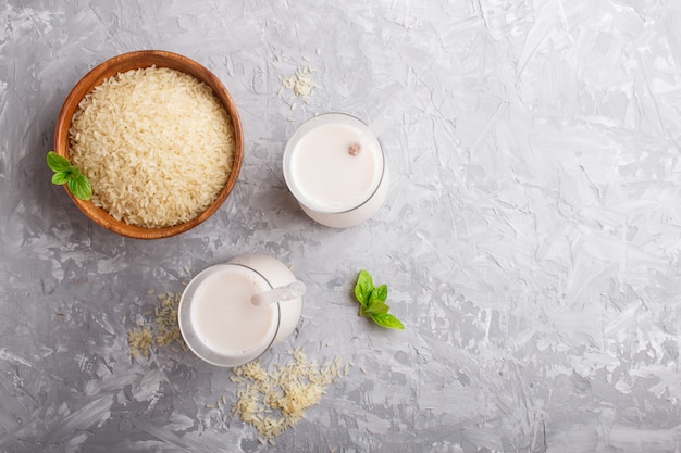 Organic non dairy rice milk in glass and wooden plate with rice seeds on a gray concrete. 