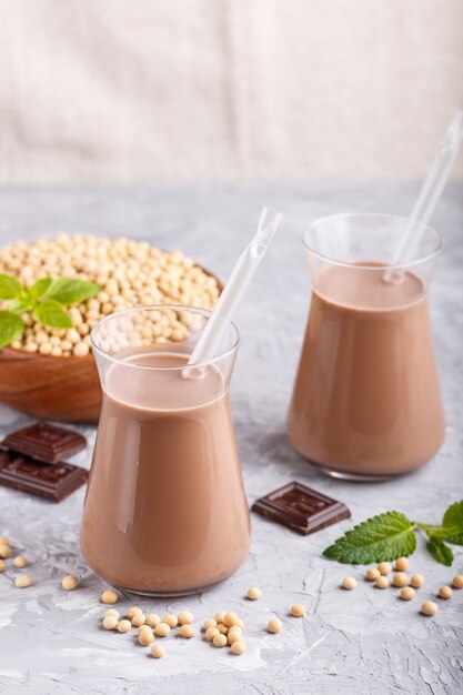 Photo organic non dairy soy chocolate milk in glass and wooden plate with soybeans on a gray concrete background. 