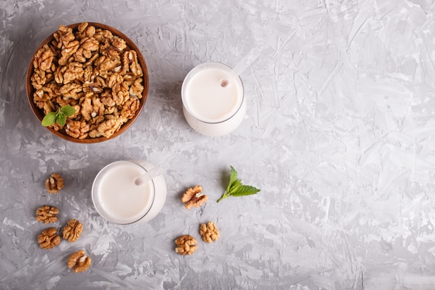 Organic non dairy walnut milk in glass and wooden plate with walnuts on a gray concrete. 