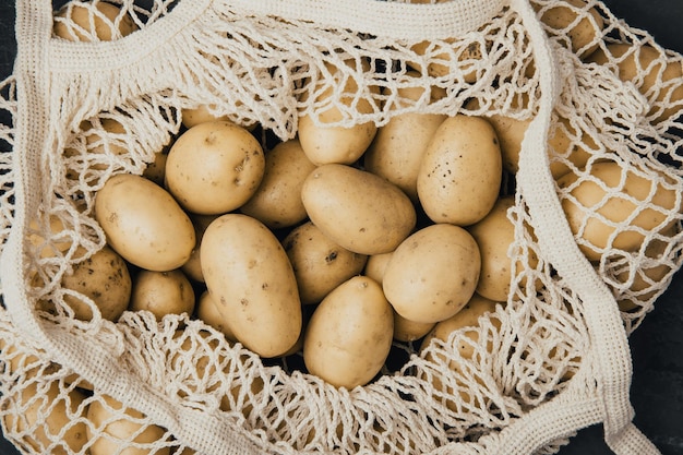 Organic potatoes Fresh raw potatoes in white cotton bag on dark background top view