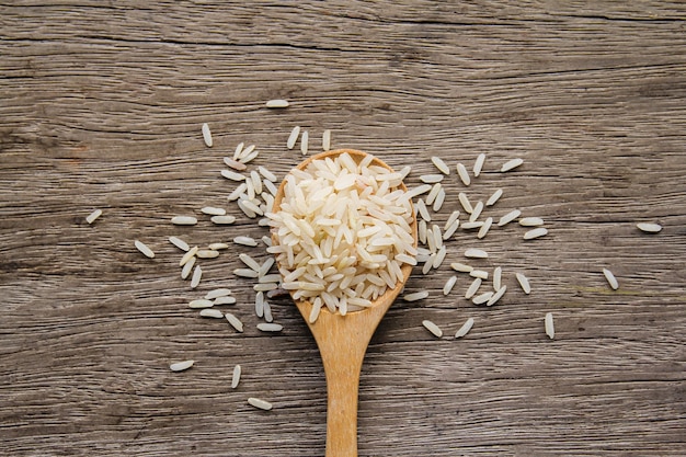 Organic raw rice in wooden spoon on old wood background