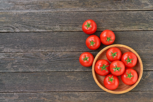 Organic red tomatoes in a wooden bowl on a rustic wooden table with copy space for text.