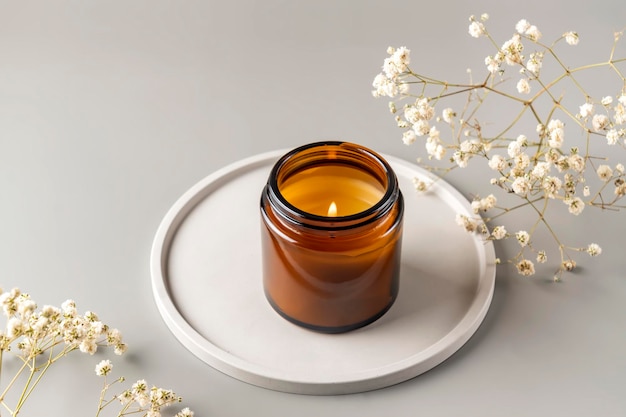 Organic scented soy candle in dark glass jar on ceramic tray minimalism concept Close up copy space for text Zero waste minimalism concept handmade candle with dry rwhite flowers